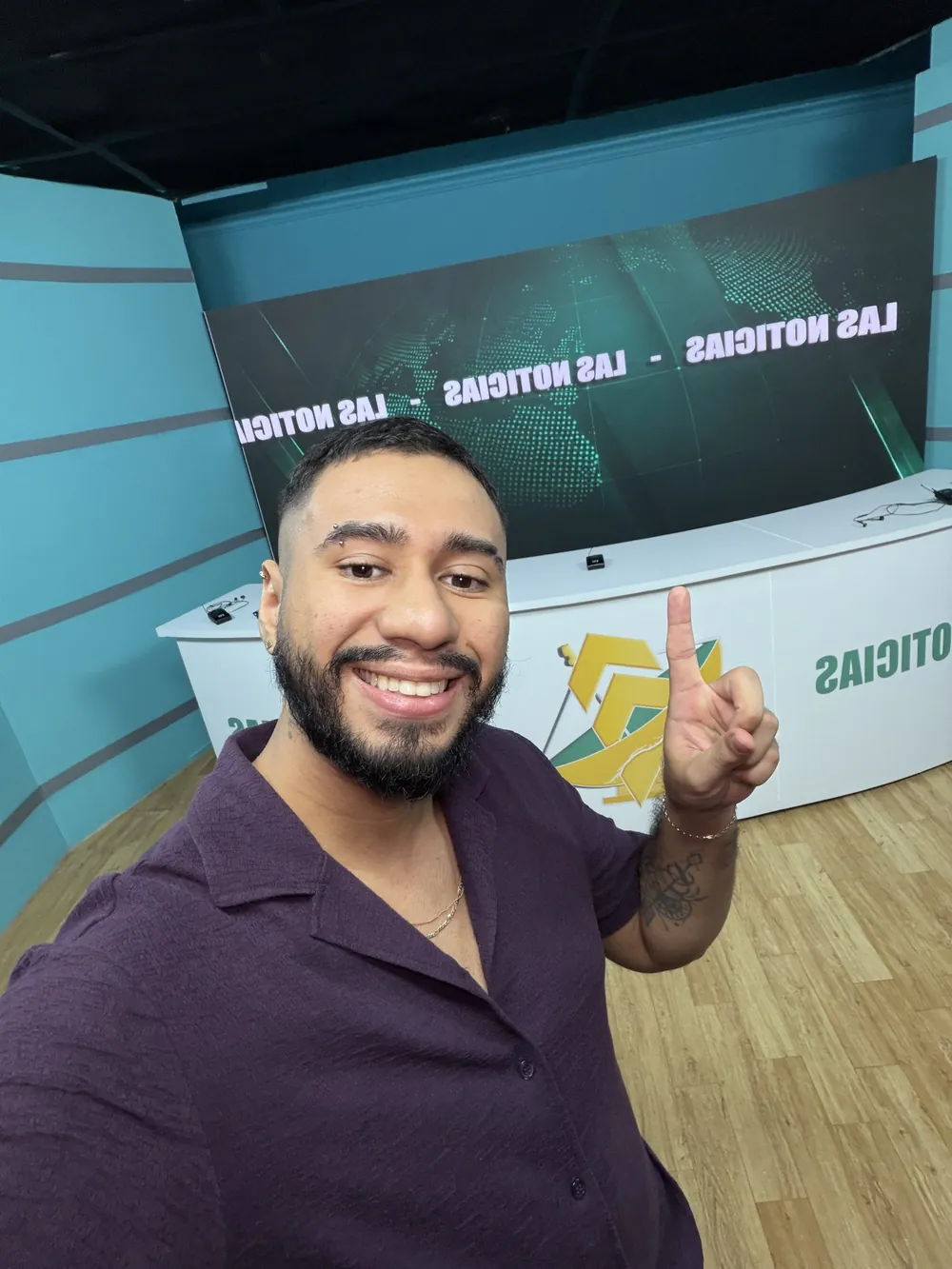 Kevin sonriendo y levantando el dedo índice en un set de televisión