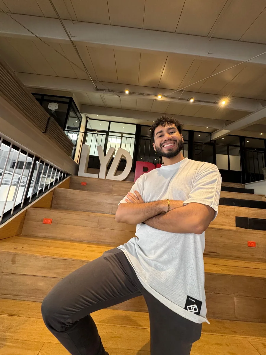Kevin sonriendo con los brazos cruzados en unas gradas de madera